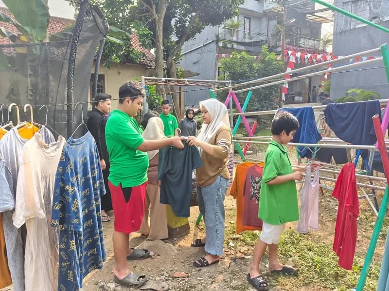 Pendamping menyerahkan pakaian kepada seorang siswa di antara rak jemuran