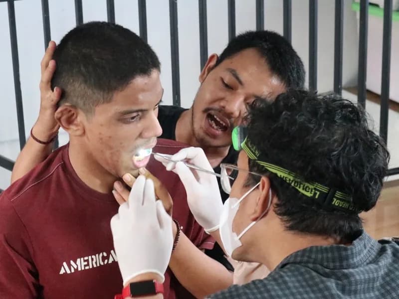 Dua petugas kesehatan memeriksa gigi seorang siswa secara bergantian